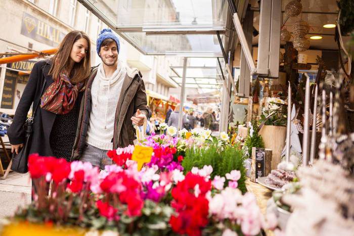 Ein junges Pärchen - Mann und Frau - schlendern über den Wiener Brunnenmarkt. Im Fordergrund ein Marktstand mit Tulpen. Foto von Stephan Doleschal.