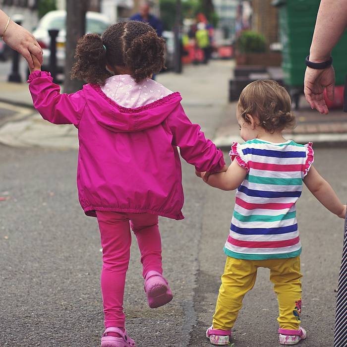 Zwei bunt angezogene Kinder gehen an der Hand ihrer Eltenrn über die Straße.