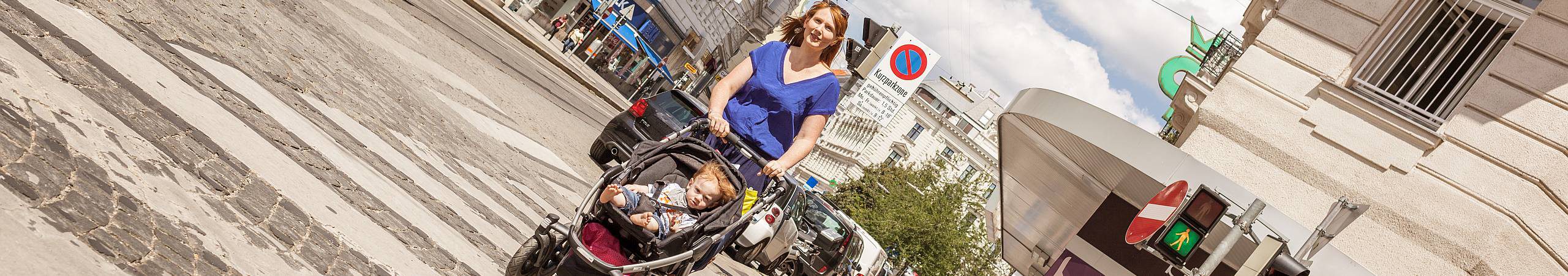 Eine junge Frau schiebt ein Buggy, in dem ein kleiner, rothaariger Bub sitz über den Zebrastreifen. Foto von Stephan Doleschal