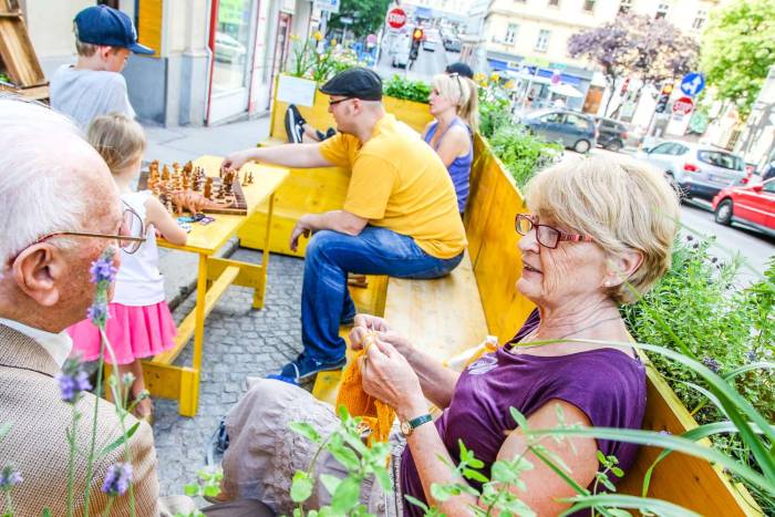 Eine Grätzloase im 7. Bezirk. Im gelben Garten, einem Parklet (Kleiner Park in der Parkspur), sitzen Leute aus der Nachbarschaft spielen, plaudern und stricken.