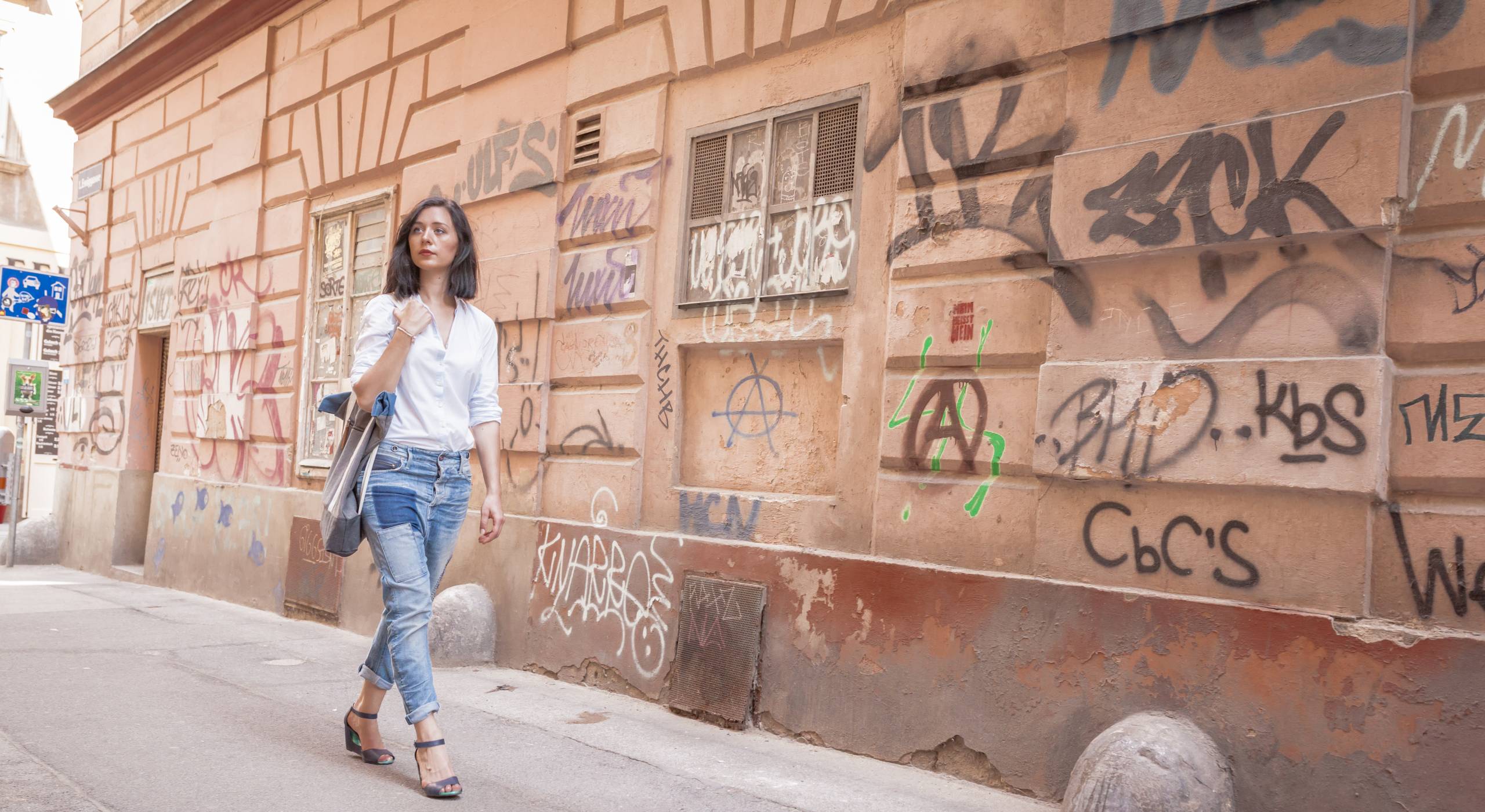 Eine junge Frau geht an einer braunen, mit GrEine junge Frau geht an einer mit Graffiti besprühten Wand vorbei. Foto von Stephan Doleschal