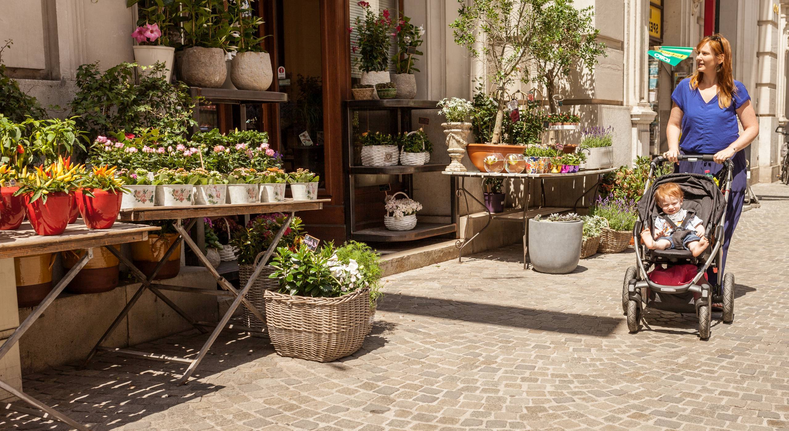 Eine junge Mutter spaziert mit ihrem einjährigen Sohn im Kinderwagen an einem Blumengeschäft vorbei. Foto von Stephan Doleschal