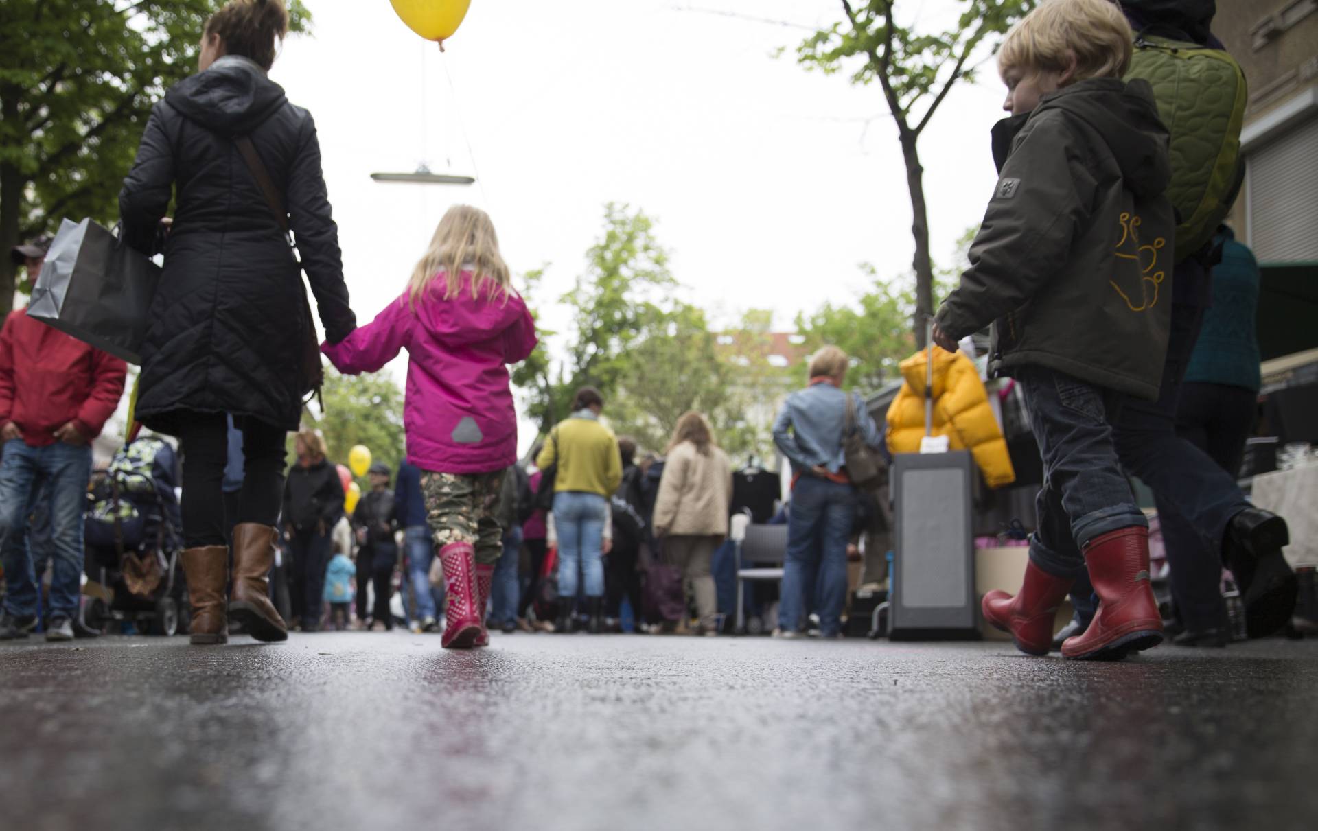 Mutter und Kind gehen Hand in Hand durch den Regen. Kind trägt Gummistiefel und rosa Regenjacke. Foto: Sebastian Philipp