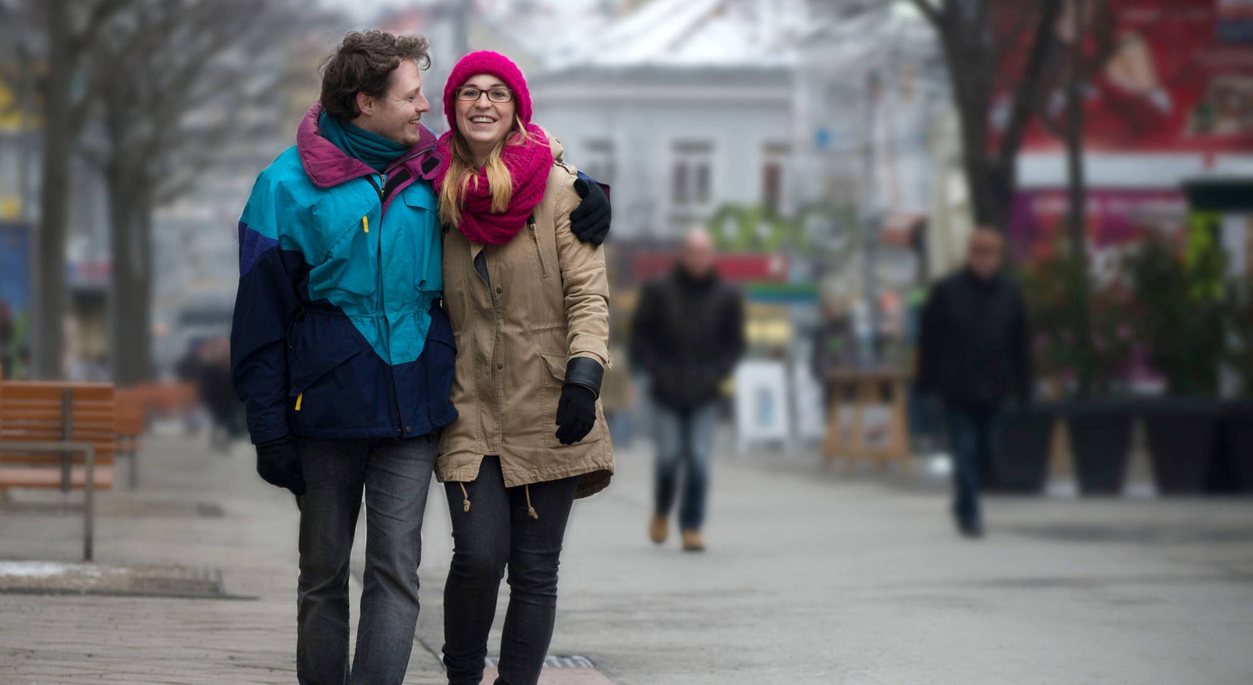 Ein junges Pärchen - Mann und Frau - geht in der winterlichen Meidlinger Hauptstraße spazieren. Er hat seinen Arm um ihre Schulter gelegt und lächelt sie verliebt an. Foto: Ernst Grünwald