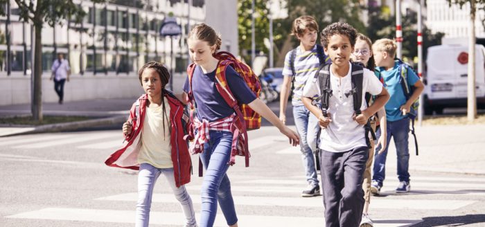 Fünf Kinder mit Rucksäcken auf dem Weg zur Schule