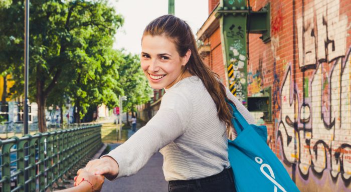 Junge Frau am Donaukanal. Sie lächelt in die Kamera und lädt zum Spazierengehen ein.