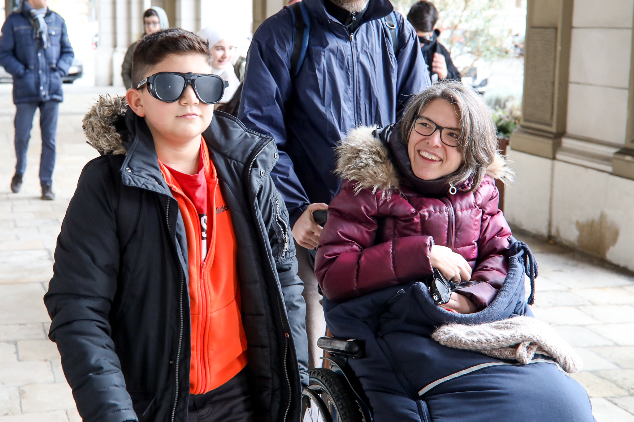 Ein Schüler geht mit einer Schlechtsehbrille. Maria Grundner, Expertin für Barrierefreiheit, fährt daneben mit dem Rollstuhl.