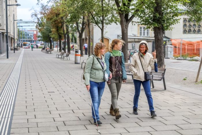 Drei Frauen gehen die Pius-Parsch-Promenade in Floridsdorf entlang. Eine von ihnen hat einen weißen Stock.