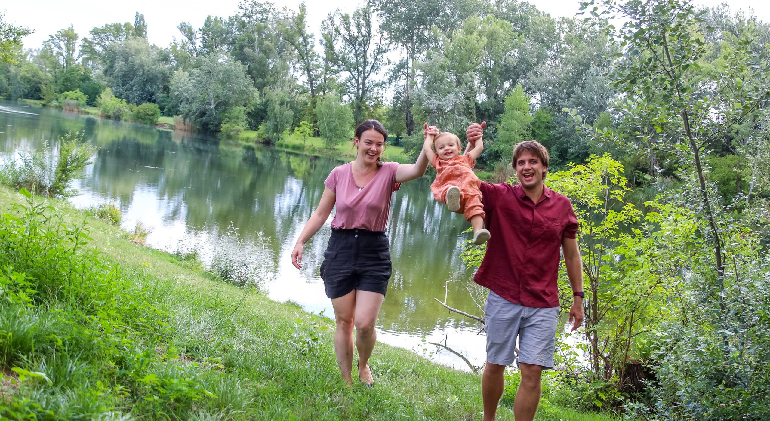 Junge Frau, Mann und Kleinkind gehen gemeinsam spazieren. Im Hintergrund ist das Mühlwasser zu sehen.