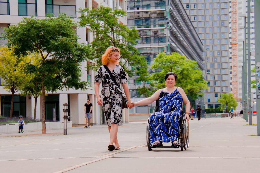 Zwei Personen, davon eine im Rollstuhl, gehen über die Donauplatte