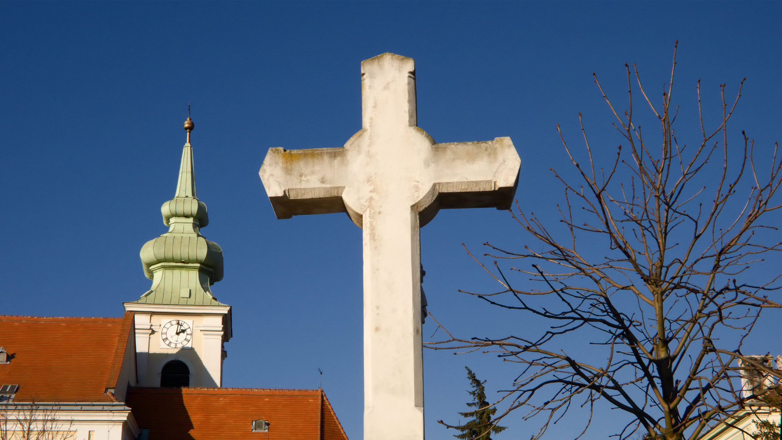 Kreuz am Leopoldauer Friedhof und Pfarrkirche im Hintergrund