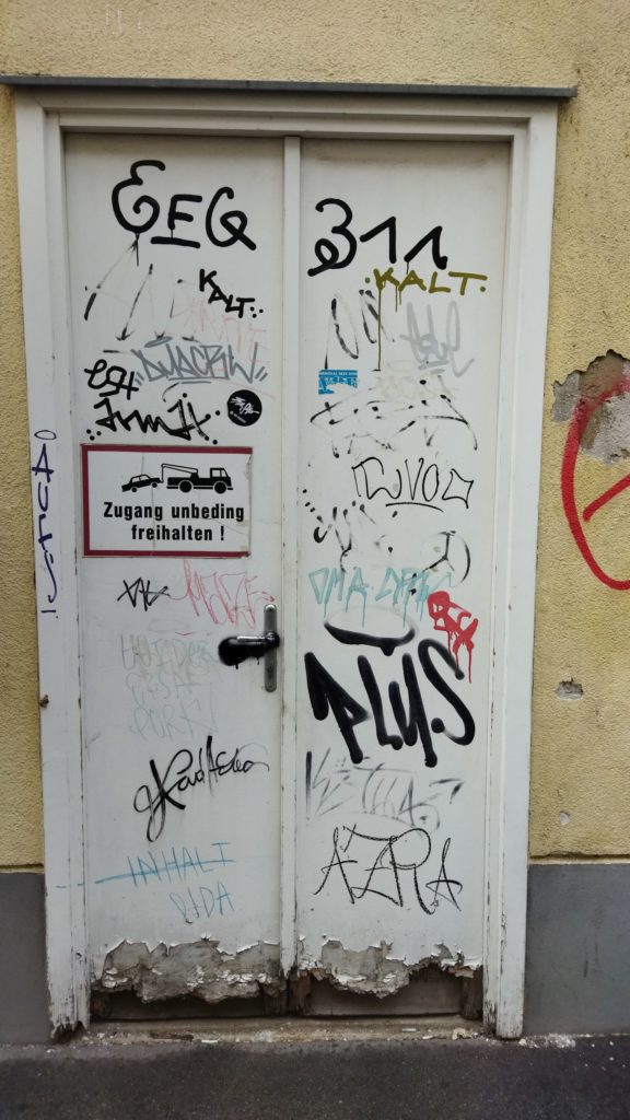 Tür mit Graffiti und Tags sowie einem Schild mit Text "Zugang unbeding freihalten!"