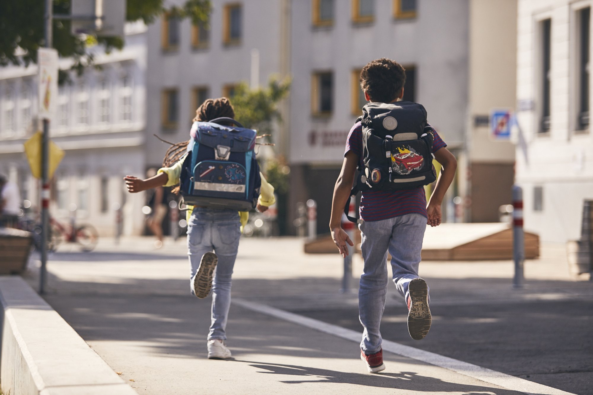 Zwei laufende Kinder von hinten, die Schultaschen haben Reflektorstreifen