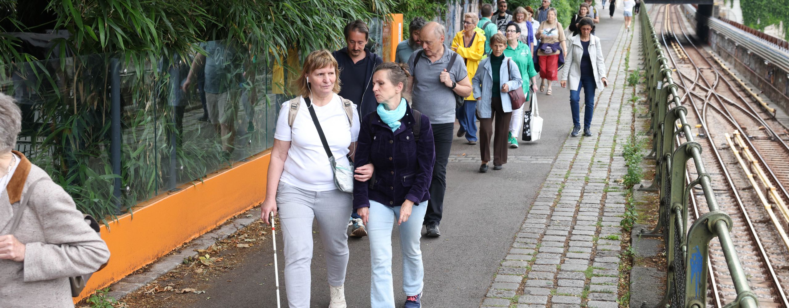 Entlang der U4-Trasse sind zahlreiche Fußgänger und Fußgängerinnen unterwegs. Eine Person im Bildvordergrund benutzt einen weißen Stock.